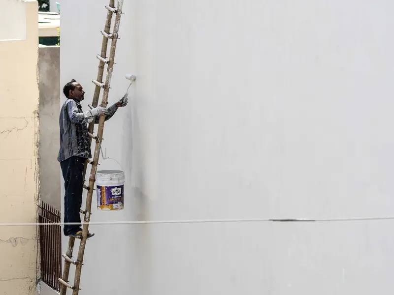 Peintre sur une échelle peignant le mur extérieur d'un bâtiment